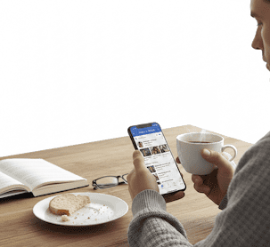 Person som sitter vid köksbordet och scrollar Facebook på mobilen med kaffekopp