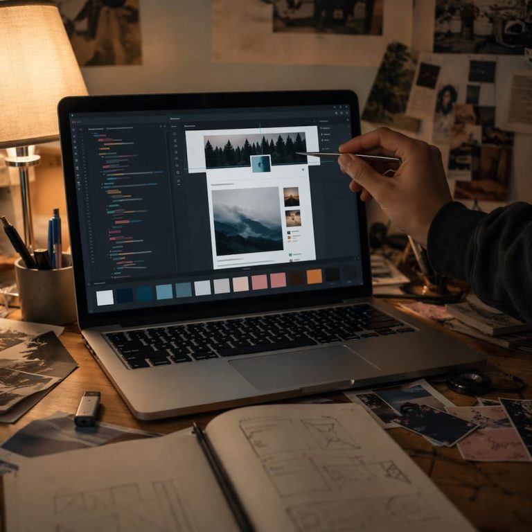 Hand med pincett som justerar en liten rubrikdel i en blogg-layout på en laptopskärm, omgiven av färgprover och skisser för temat
